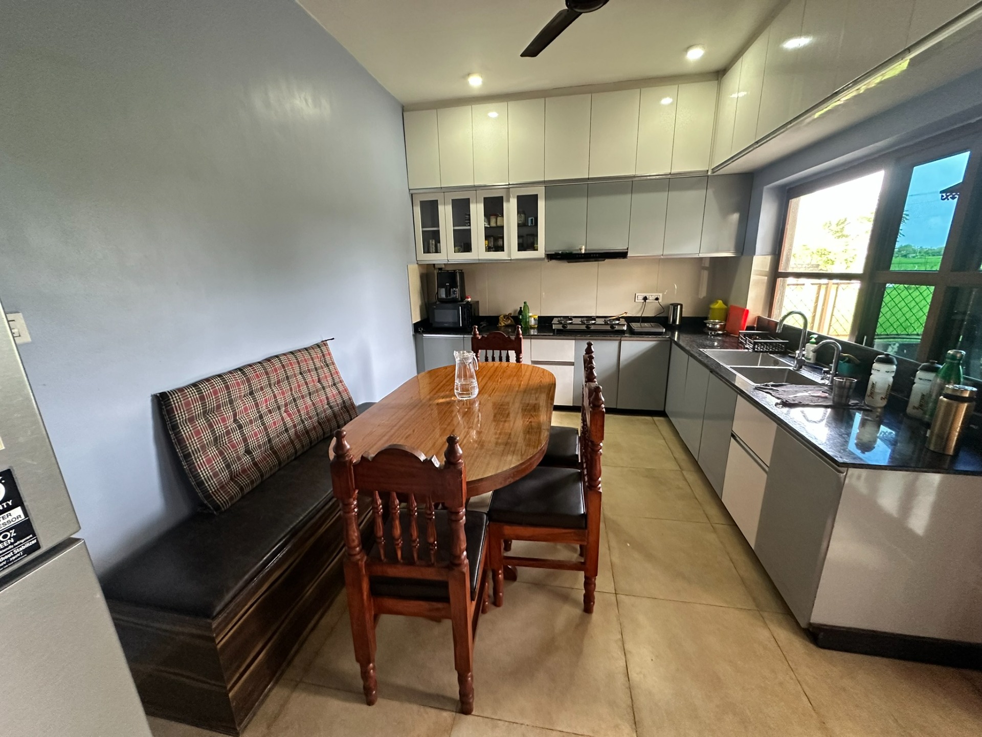 Moderne keuken met witte kasten, houten eettafel, stoelen, spoelbak en uitzicht via raam.